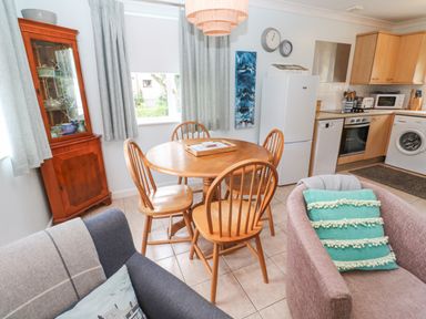 A kitchen and dining area with a round wooden table and four chairs a refrigerator washing machine and wooden cabinets at Chy Lowena Goldenbank near Budock Water