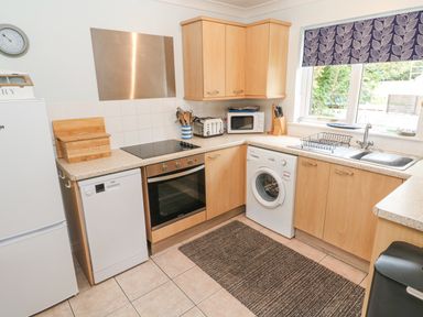 A kitchen with wooden cabinets a stove oven microwave washing machine and sink with window at Chy Lowena Goldenbank near Budock Water