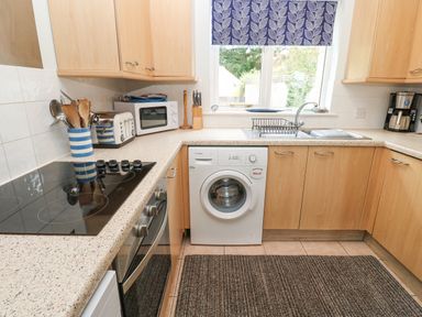 A kitchen with wooden cabinets a washing machine oven microwave and a window with a patterned blind at Chy Lowena Goldenbank near Budock Water