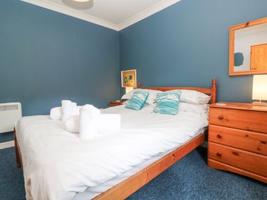 A bedroom with a double bed white bed linens blue pillows wooden dresser and mirror at Chy Lowena Goldenbank near Budock Water