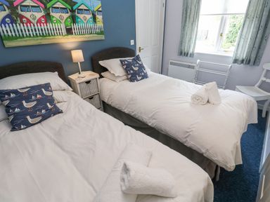A bedroom with two single beds white bedding and blue pillows a small bedside table with a lamp a painting of colorful vans on the wall at Chy Lowena Goldenbank near Budock Water