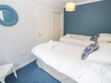 A bedroom with two beds with white bedding a blue feature wall a round blue mirror and a white sliding door closet at Chy Lowena in Goldenbank near Budock Water