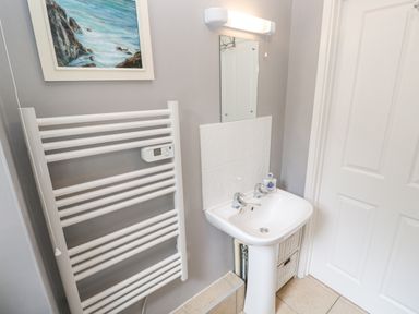 A bathroom with a white sink, towel radiator, mirror, and a painting above the radiator at Chy Lowena Goldenbank near Budock Water