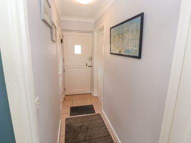 A hallway with two rugs on the floor a white wooden door at the end and framed pictures on the walls at Chy Lowena Goldenbank near Budock Water