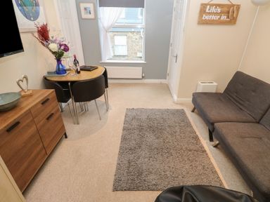 A living room with gray sofa dining table chairs and a wooden cabinet at 5 Lyonesse Apartments in St Ives