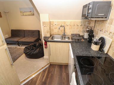 A kitchen with a sink stove microwave and utensils next to a living area with a sofa black bean bag and lamp at 5 Lyonesse Apartments in St Ives
