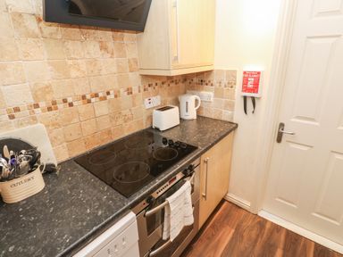 A kitchen countertop with a stove, oven, toaster, kettle, cutlery holder, and fire blanket on the wall at 5 Lyonesse Apartments in St Ives