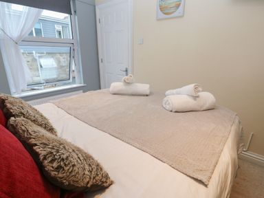 A bedroom with a bed with towels on it and a window with curtains at 5 Lyonesse Apartments in St Ives