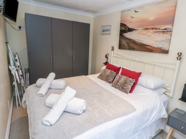 A bedroom with a bed with pillows and towels and a wardrobe and a wall-mounted television at 5 Lyonesse Apartments in St Ives