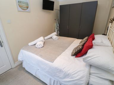 A bedroom with a bed with pillows and towels a wardrobe a wall-mounted television and an ironing board at 5 Lyonesse Apartments in St Ives