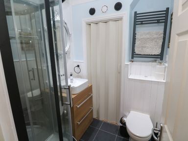 A small bathroom with a shower enclosure a sink with wooden drawers a toilet and a folding door at 5 Lyonesse Apartments in St Ives