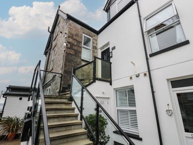 An exterior view of a building with stairs leading to a black door and windows with glass railings at 5 Lyonesse Apartments in St Ives