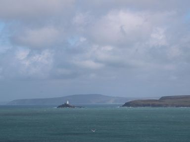 A coastal scene with a lighthouse on a small island and land in the background at 5 Lyonesse Apartments in St Ives