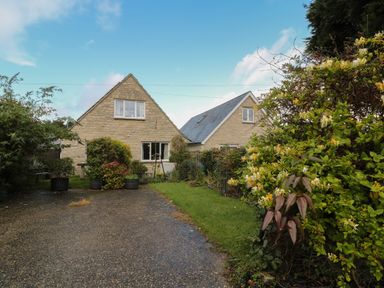 A gravel driveway with shrubs and two stone houses in the background at Old Harry Cottage 16 in Swanage
