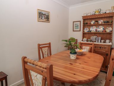 A dining room with a wooden table and chairs a plant and bowl on the table and a wooden cupboard with plates at Old Harry Cottage 16 in Swanage