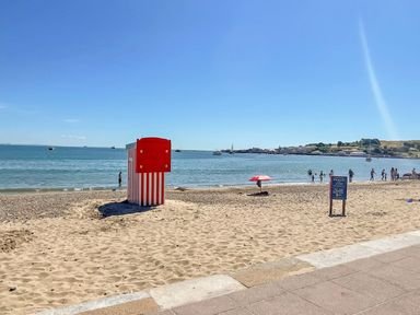 A sandy beach with a red and white striped beach hut and people near the water at Old Harry Cottage 16 Swanage