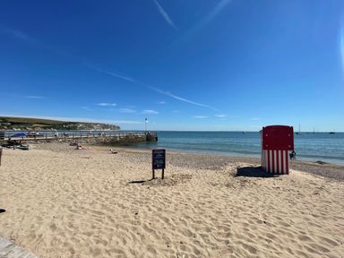 A sandy beach with a red and white striped hut and a pier in the background at Old Harry Cottage 16 Swanage