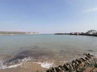 A coastal scene showing a beach with pebbles and rocks a pier extending into the sea and cliffs in the distance at Old Harry Cottage 16 Swanage