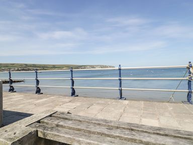 A wooden bench on a stone pier with metal railings overlooking the sea and distant hills at Old Harry Cottage 16 Swanage