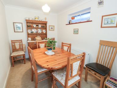 A dining room with a wooden table and chairs a wooden cabinet with dishes framed pictures on the walls and a small window at Old Harry Cottage 16 in Swanage