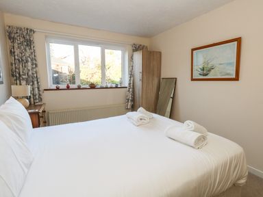 A bedroom with a bed and rolled towels bedside table with a lamp wardrobe and a framed picture on the wall at Old Harry Cottage 16 in Swanage