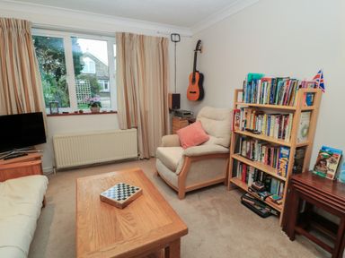 A living room with an armchair, bookshelf, guitar on the wall, coffee table, television, and window at Old Harry Cottage 16 in Swanage