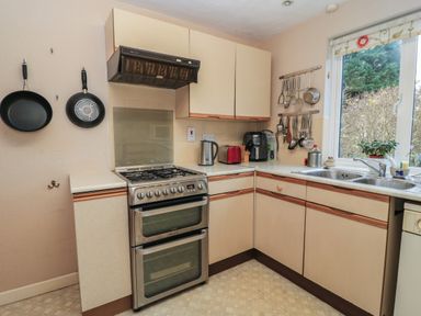 A kitchen with a stove oven sink window and utensils hanging on the wall at Old Harry Cottage 16 Swanage