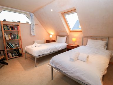 A bedroom with two single beds bedside tables with lamps and a bookshelf at Old Harry Cottage 16 in Swanage
