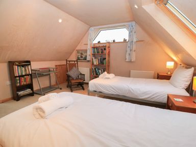 A bedroom with two single beds a wooden chair bookshelves and a small desk at Old Harry Cottage 16 in Swanage
