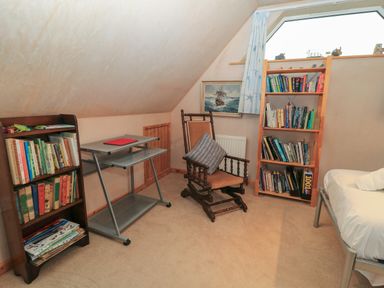 A small attic room with bookshelves a rocking chair a small desk and a single bed at Old Harry Cottage 16 Swanage