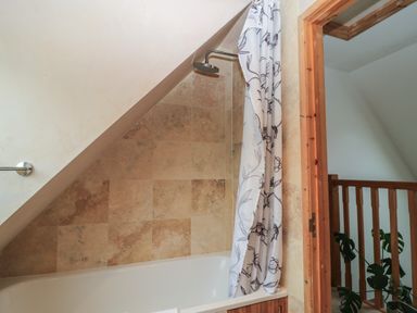 A bathroom with a bathtub and shower under a sloped ceiling at Old Harry Cottage 16 in Swanage