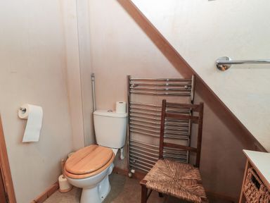 A bathroom with a toilet wooden seat a wooden chair a towel rack and toilet paper rolls at Old Harry Cottage 16 in Swanage