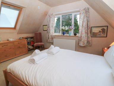 A bedroom with a bed with white sheets and towels a wooden dresser a striped chair a window with floral curtains and flowers on the windowsill at Old Harry Cottage 16 Swanage