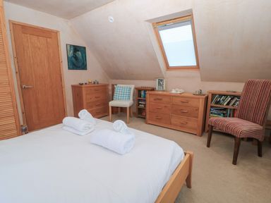 A bedroom with a bed holding rolled towels wooden furniture including dressers and bookshelves two chairs and a slanted window at Old Harry Cottage 16 Swanage