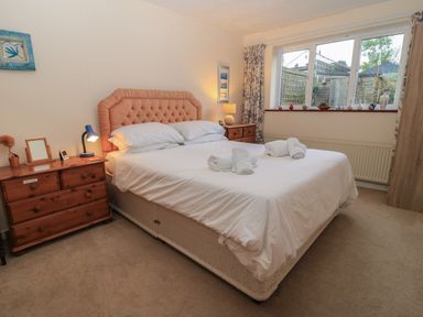 A bedroom with a double bed with a padded headboard two wooden nightstands with lamps and decorative items and a large window at Old Harry Cottage 16 in Swanage