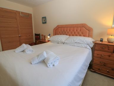 A bedroom with a large bed with white sheets and towels on top two wooden bedside tables with lamps and a wooden closet at Old Harry Cottage 16 Swanage