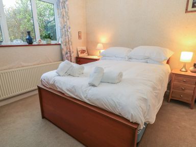 A bedroom with a double bed with folded towels bedside tables with lamps and a window with curtains at Old Harry Cottage 16 Swanage