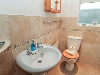 A bathroom with a pedestal sink a toilet with wooden seat and a wall-mounted cabinet at Old Harry Cottage 16 Swanage