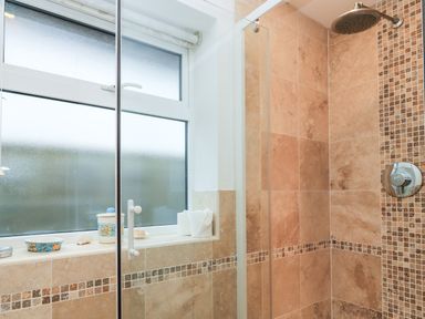 A tiled shower with a glass door and a window with items on the windowsill at Old Harry Cottage 16 Swanage