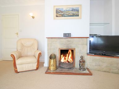 A living room with an armchair a fireplace with a fire a television and a painting above the fireplace at Artists Cottage in Minffordd near Penrhyndeudraeth