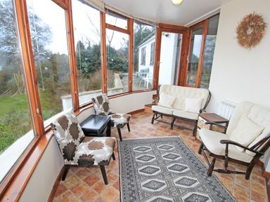 A sunroom with floral patterned chairs a cushioned loveseat armchair and a patterned rug at Artists Cottage in Minffordd near Penrhyndeudraeth