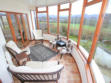 A sunroom with wooden framed windows cushioned wooden chairs a patterned rug and tiled floor at Artists Cottage in Minffordd near Penrhyndeudraeth