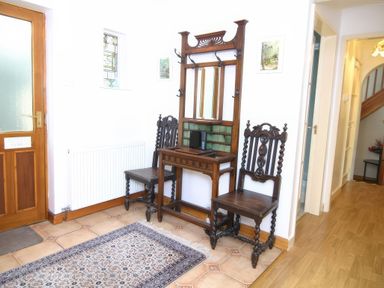 An entrance hallway with wooden door two dark wooden chairs a mirror with hooks a patterned rug and tiled floor at Artists Cottage in Minffordd near Penrhyndeudraeth