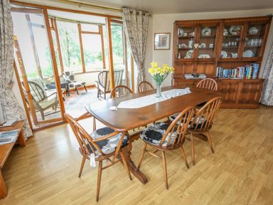 A dining room with a wooden table and chairs a vase with flowers and a china cabinet at Artists Cottage in Minffordd near Penrhyndeudraeth