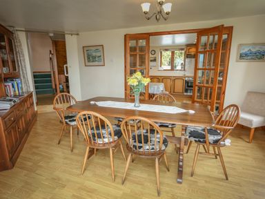 A dining room with a wooden table and six chairs with cushions and flowers on the table at Artist's Cottage in Minffordd near Penrhyndeudraeth