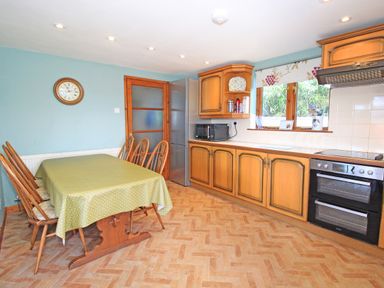 A kitchen with wooden cabinets a dining table with chairs and a clock on the wall at Artists Cottage in Minffordd near Penrhyndeudraeth