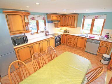 A kitchen with wooden cabinets a dining table with a green polka dot tablecloth and windows at Artists Cottage in Minffordd near Penrhyndeudraeth