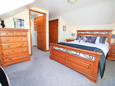 A bedroom with a wooden bed and dresser next to a door leading to a bathroom at Artists Cottage in Minffordd near Penrhyndeudraeth