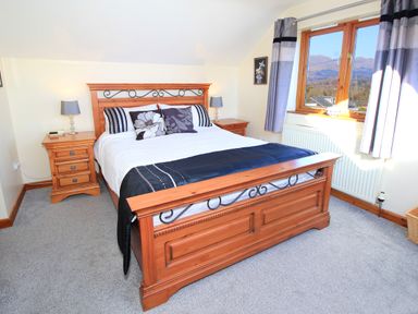A bedroom with a wooden bed frame two bedside tables with lamps a window with curtains and a radiator at Artists Cottage in Minffordd near Penrhyndeudraeth