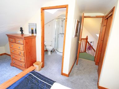 A bedroom with a wooden chest of drawers a small bathroom and a hallway with stairs at Artists Cottage in Minffordd near Penrhyndeudraeth